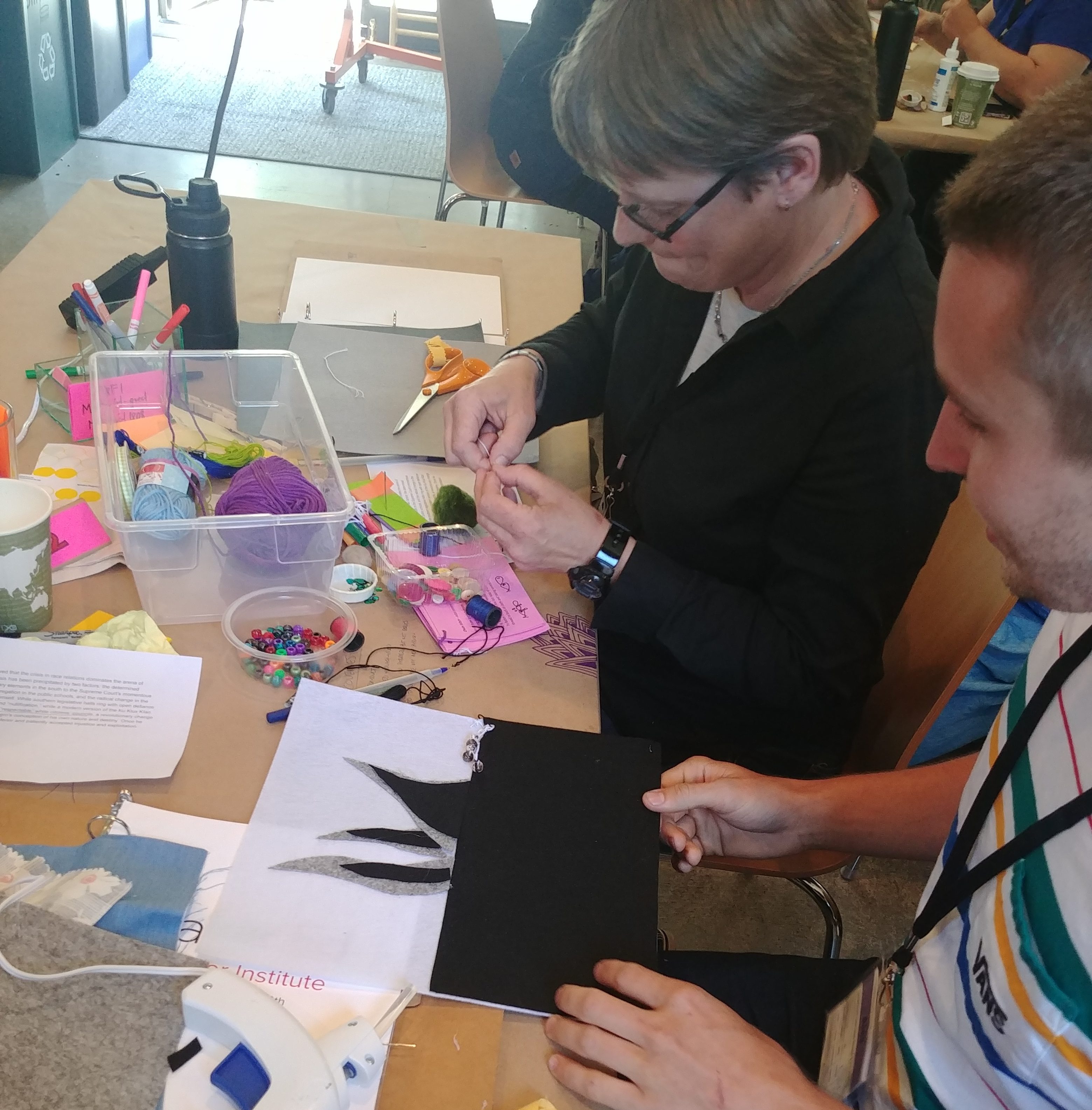 Two educators, a man and a woman, collaborate on a hand-sewn quilt block.